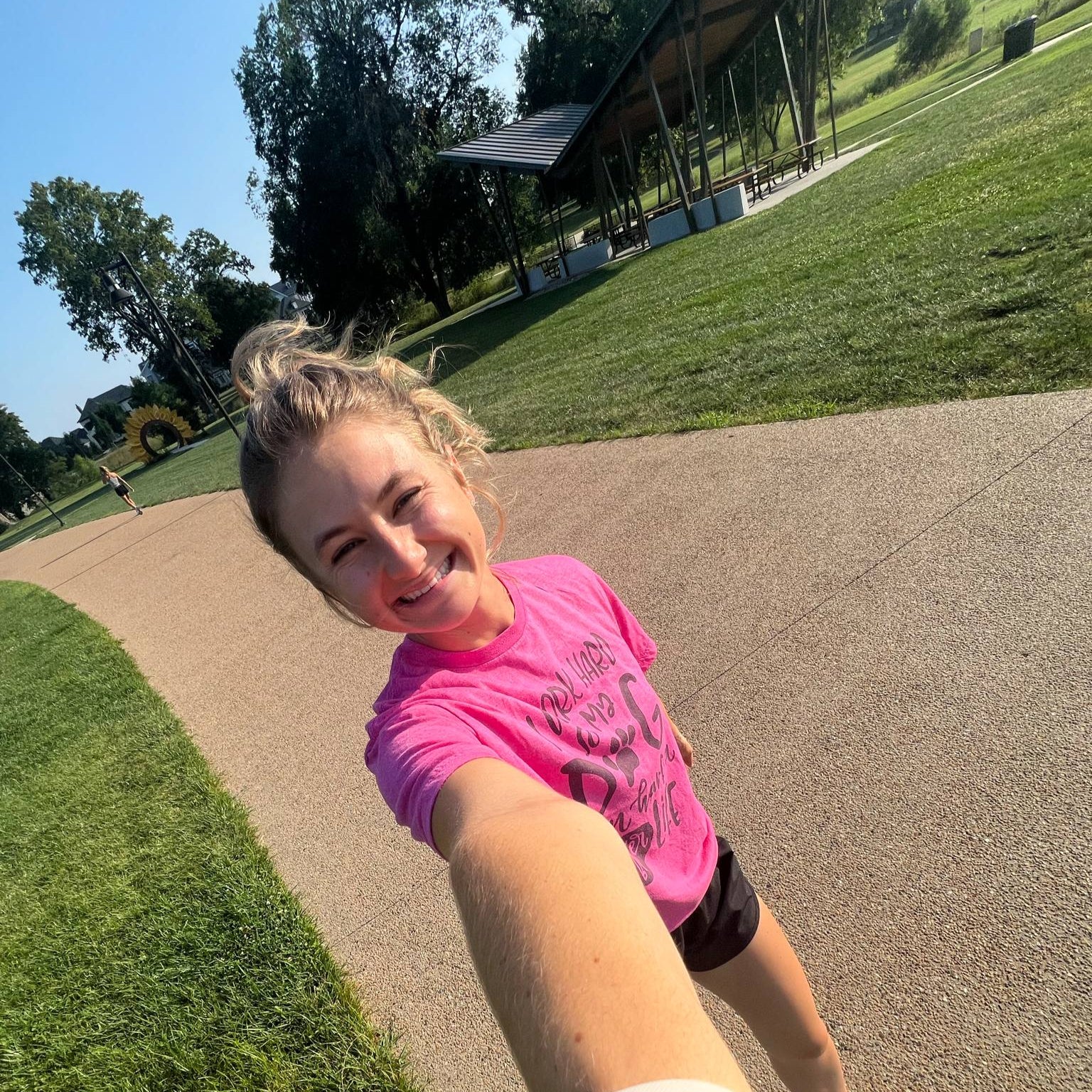 Person in a pink shirt taking a selfie outdoors on a sunny day