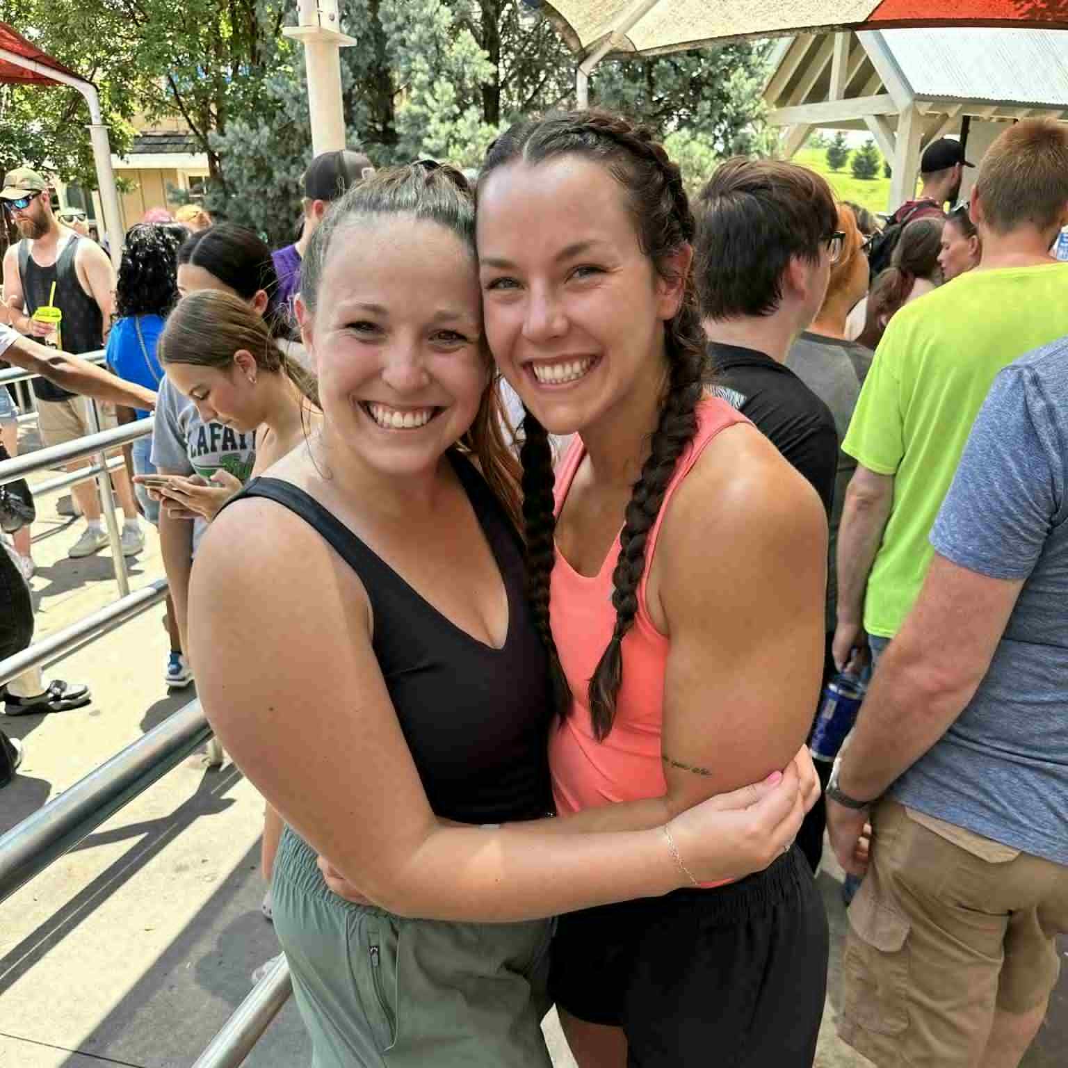 Two women hugging at an outdoor event with people and trees in the background